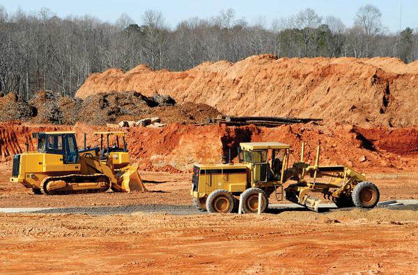 Construction equipment working on a clear-cut site consisting of no vegetation and red clay.